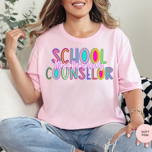 May include: A pink t-shirt with the text "SCHOOL COUNSELOR" in colorful letters. The text "Mrs. Kennedy" is written in smaller letters below the main text.