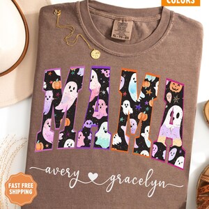 May include: Espresso-colored t-shirt with the word "MAMA" in a Halloween-themed design. The letters are filled with ghosts, pumpkins, and stars. The names "avery" and "gracelyn" are written below the word "MAMA".
