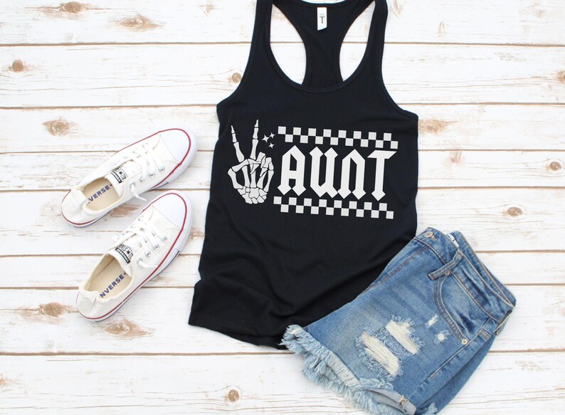 May include: Black tank top with a white skeleton hand making a peace sign and the word "AUNT" in a gothic font with a checkered pattern behind it.