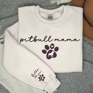 May include: A white sweatshirt with the text "pitbull mama" and a paw print with a heart and a pitbull silhouette. The sleeve has the text "Bella Max" and a paw print.