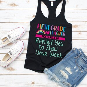K&ouml;nnte beinhalten: Schwarzes Tanktop mit dem Text "Fifth Grade Teacher Most Likely To Remind You To Show Your Work" in bunten Buchstaben mit einem Regenbogen und einem Herz-Motiv.