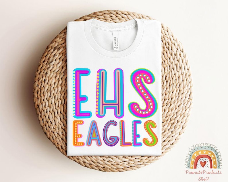 Puede incluir: Camiseta blanca con el texto "EHS Eagles" en letras de colores y contorneadas. Las letras est&aacute;n decoradas con peque&ntilde;os puntos.
