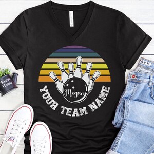 K&ouml;nnte beinhalten: Schwarzes V-Ausschnitt-T-Shirt mit einem Retro-Design mit Bowling-Pins und einer Bowlingkugel. Der Text "Your Team Name" ist um das Design herum geschrieben, mit dem Namen "Megan" auf der Bowlingkugel.