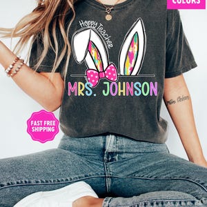 May include: A gray t-shirt with a white bunny ear design and the text "Hoppy Teacher" and "MRS. JOHNSON" in rainbow colors.