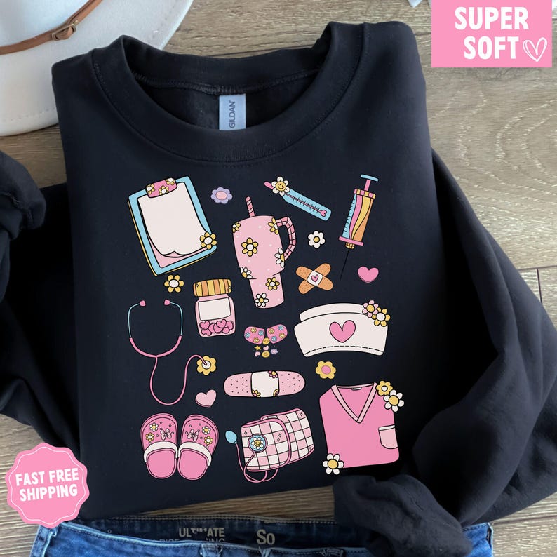May include: Black sweatshirt with a colorful, floral-themed medical illustration. The design includes a stethoscope, pills, bandages, a nurse's cap, and a pink tumbler. The words "SUPER SOFT" are in a pink box.