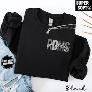 May include: Black crewneck sweatshirt with the text "RDMS Ashley" in gray and white. A silver necklace is draped across the front. The words "Super Soft" are in the upper right corner.