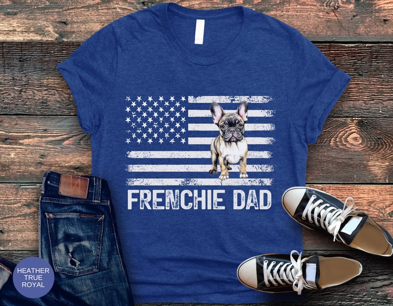 May include: A blue t-shirt with a distressed American flag design featuring a French Bulldog. The text "FRENCHIE DAD" is printed below the flag.