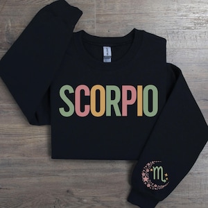 May include: Black sweatshirt with the word "SCORPIO" in colorful letters and a small moon and star design with the letter "m" on the sleeve.