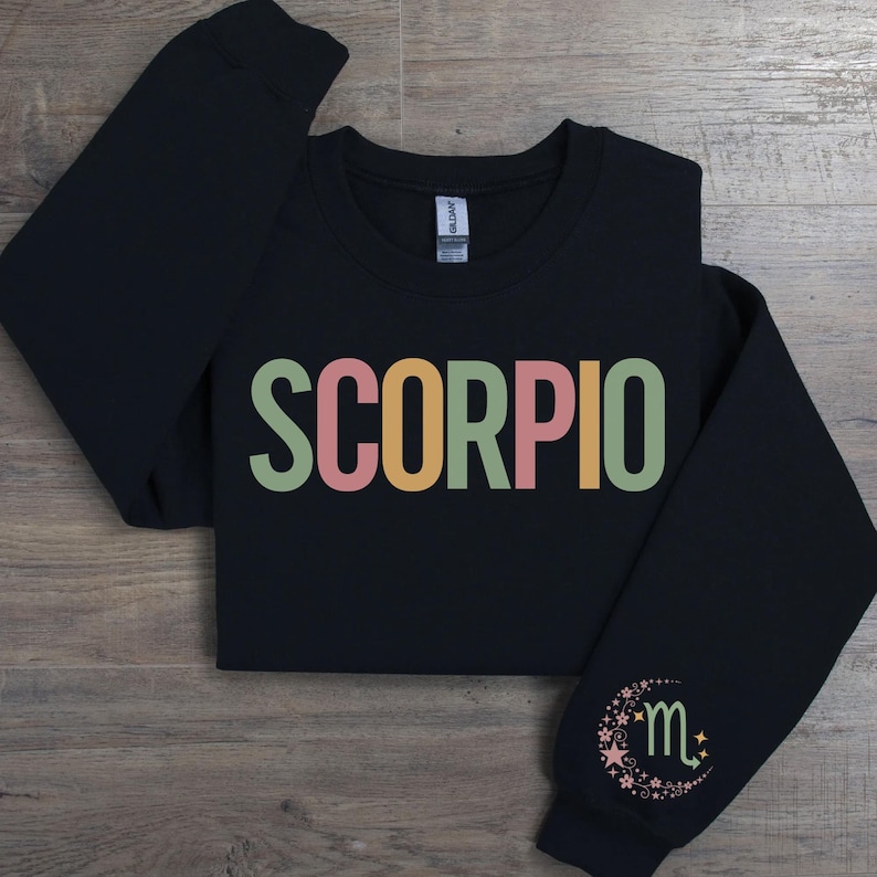 May include: Black sweatshirt with the word "SCORPIO" in colorful letters and a small moon and star design with the letter "m" on the sleeve.