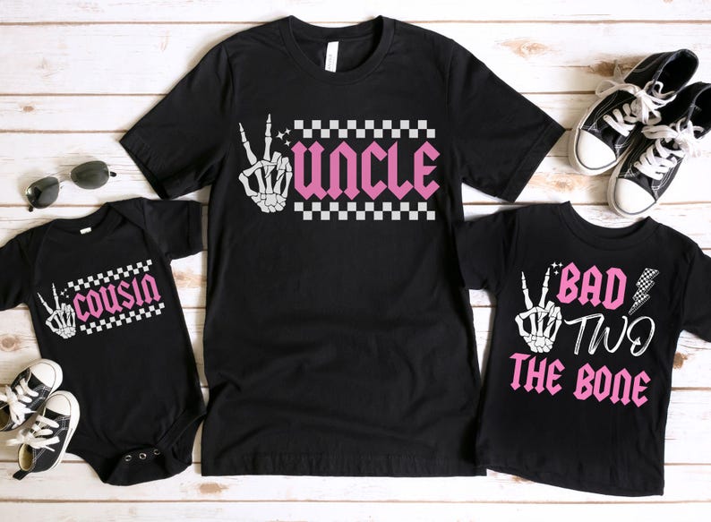 K&ouml;nnte beinhalten: Drei schwarze T-Shirts mit einem karierten Muster und einer Skeletthand. Die Shirts sagen "Onkel", "Cousin" und "Bad Two The Bone".