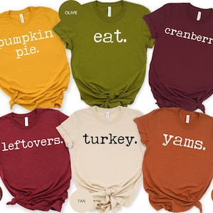 May include: Six different colored t-shirts with Thanksgiving themed text printed in white on each shirt. The shirts are mustard yellow, olive green, maroon, heather cardinal, tan, and autumn.