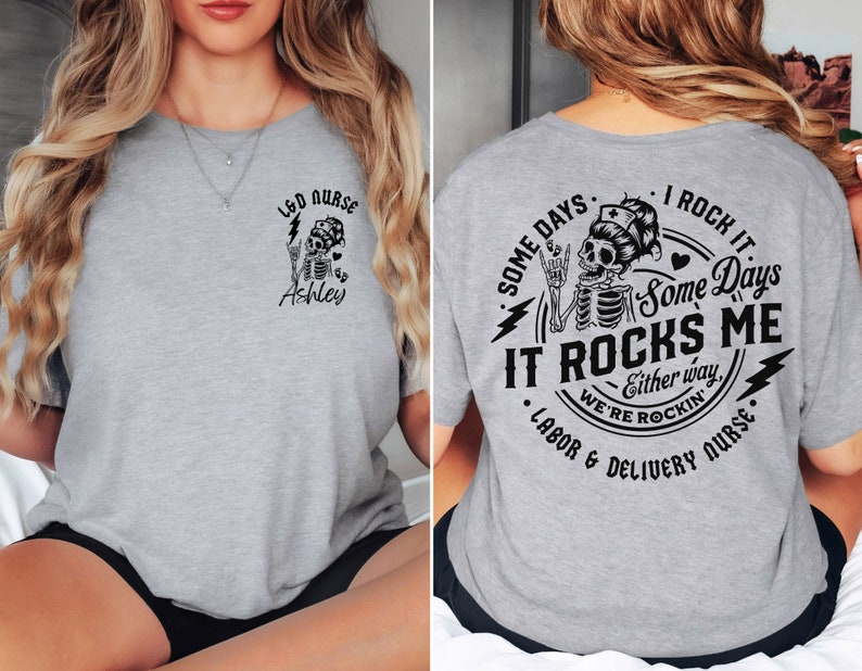 K&ouml;nnte beinhalten: Graues T-Shirt mit einem Skelett-Motiv und dem Text "LED NURSE Ashley" auf der Vorderseite und "SOME DAYS I ROCK IT Some Days IT ROCKS ME Either way WE'RE ROCKIN' LABOR & DELIVERY NURSE" auf der R&uuml;ckseite.