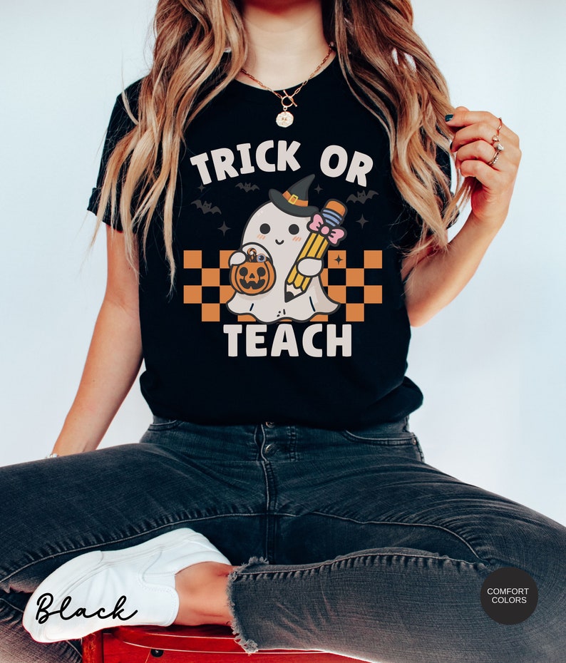K&ouml;nnte beinhalten: Schwarzes T-Shirt mit einem Grafikdruck eines Geistes, der einen Hexenhut tr&auml;gt und einen Bleistift und einen K&uuml;rbis h&auml;lt. Der Text "Trick or Teach" ist auf dem T-Shirt aufgedruckt.