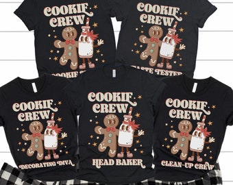 May include: Four black t-shirts with a gingerbread man and milk bottle design. The shirts have the text "Cookie Crew" and different roles like "Head Baker", "Decorating Diva", "Clean-Up Crew", and "Taste Tester".