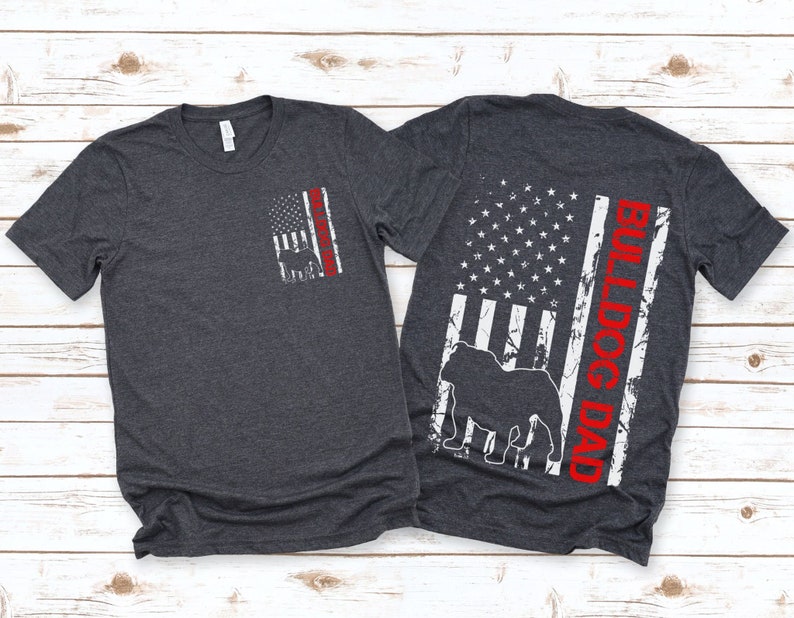 May include: Two dark heather grey t-shirts with a distressed American flag design. One shirt has a bulldog silhouette and the text "Bulldog Dad" in red. The other shirt has a smaller distressed American flag with a bulldog silhouette.