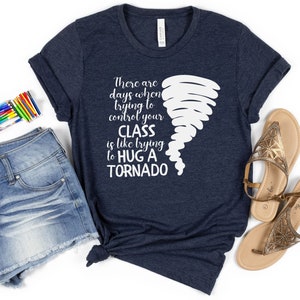 May include: A navy blue t-shirt with a white graphic of a tornado and the text "There are days when trying to control your CLASS is like trying to HUG A TORNADO".