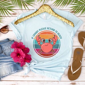 May include: A light blue t-shirt with a retro-style graphic of a crab with the text "If Crabby Please Return to Beach".