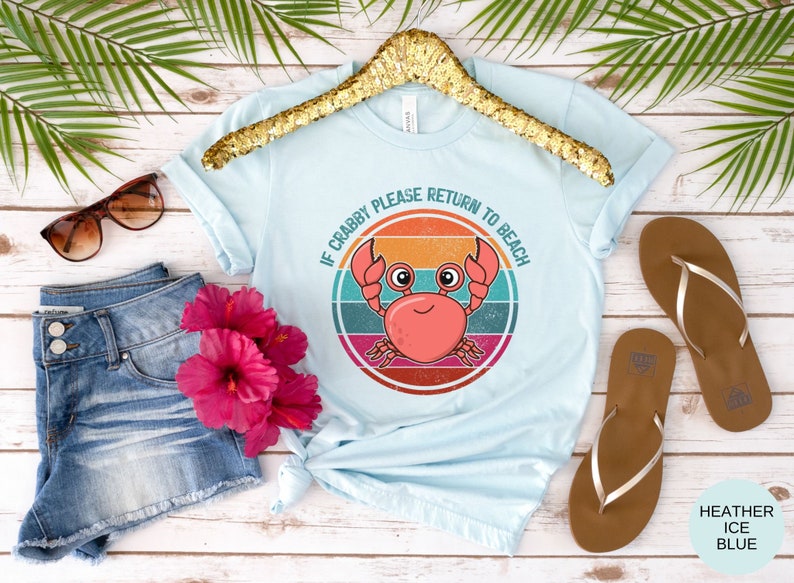 May include: A light blue t-shirt with a retro-style graphic of a crab with the text "If Crabby Please Return to Beach".