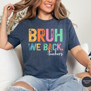 May include: A heather navy blue t-shirt with the text "BRUH WE BACK. -teachers" in rainbow colors. The text has a distressed, vintage look.