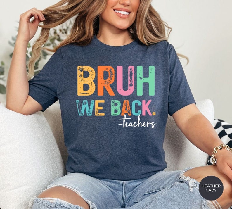May include: A heather navy blue t-shirt with the text "BRUH WE BACK. -teachers" in rainbow colors. The text has a distressed, vintage look.