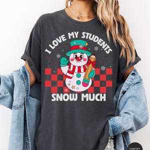 May include: A dark gray t-shirt with a snowman holding a pencil and the text "I love my students snow much".