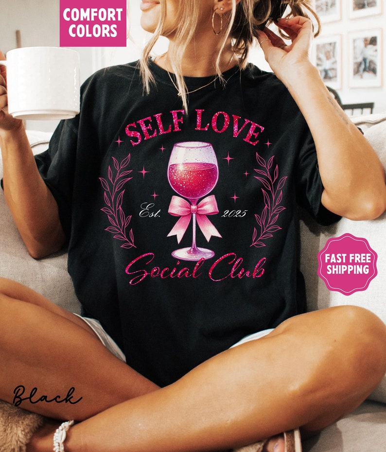 May include: Black t-shirt with pink glitter text that reads "Self Love Social Club" with a pink glitter wine glass and bow. The text "Est. 2025" is also included.