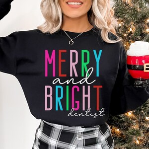 May include: Black sweatshirt with the text "Merry and Bright dentist" in colorful letters. The text is in a rainbow color scheme.