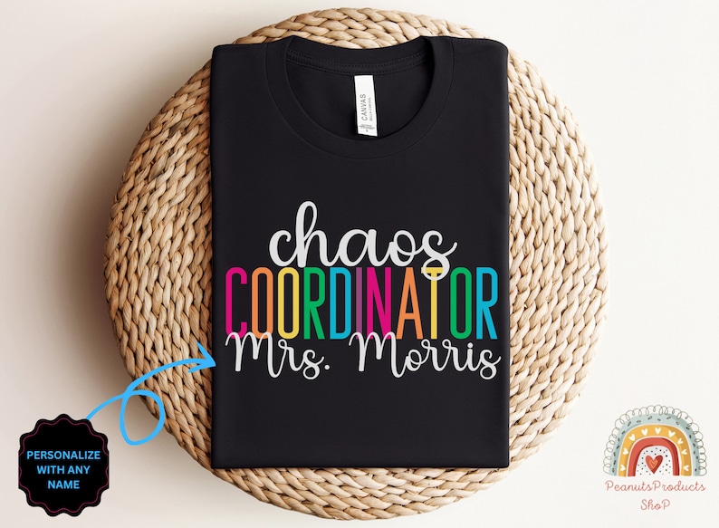 Pu&ograve; includere: Maglietta nera con il testo "chaos coordinator Mrs. Morris" in colori arcobaleno. Il testo &egrave; su una maglietta nera. La maglietta &egrave; piegata e mostrata su un cesto intrecciato.
