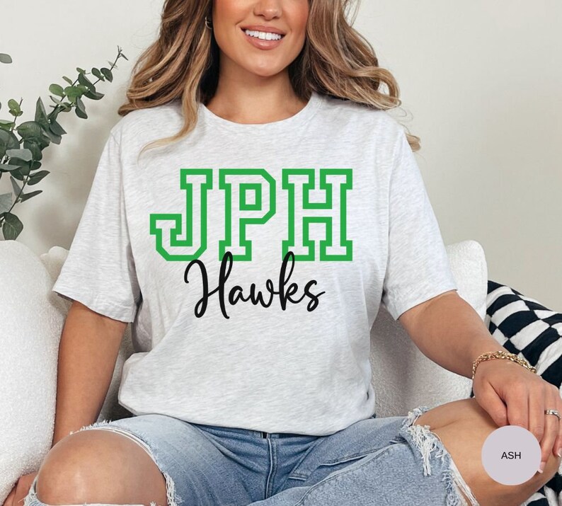 May include: A gray t-shirt with a green and white "JPH Hawks" graphic print.