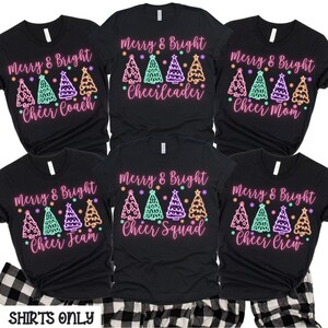 Pu&ograve; includere: Set di sei magliette nere con un testo rosa "Merry & Bright" e disegni di alberi di Natale verde neon, viola e arancio. Le magliette hanno testi diversi sotto gli alberi, tra cui "Cheer Coach", "Cheerleader", "Cheer Mom", "Cheer Team", "Cheer Squad" e "Cheer Crew".