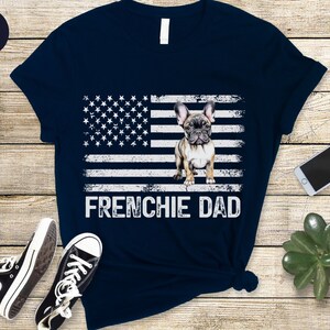 May include: Navy blue t-shirt with a distressed American flag design and a French bulldog graphic. The text "Frenchie Dad" is printed below the flag.