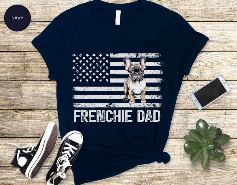May include: Navy blue t-shirt with a distressed American flag design and a French bulldog graphic. The text "Frenchie Dad" is printed below the flag.
