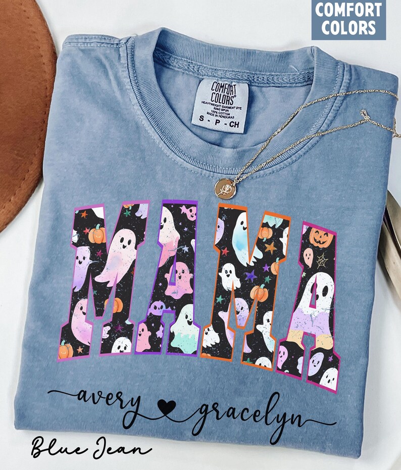 May include: Blue jean colored t-shirt with the word "MAMA" in a Halloween-themed design. The letters are filled with ghosts, pumpkins, and stars. The names "avery" and "gracelyn" are written below the word "MAMA".