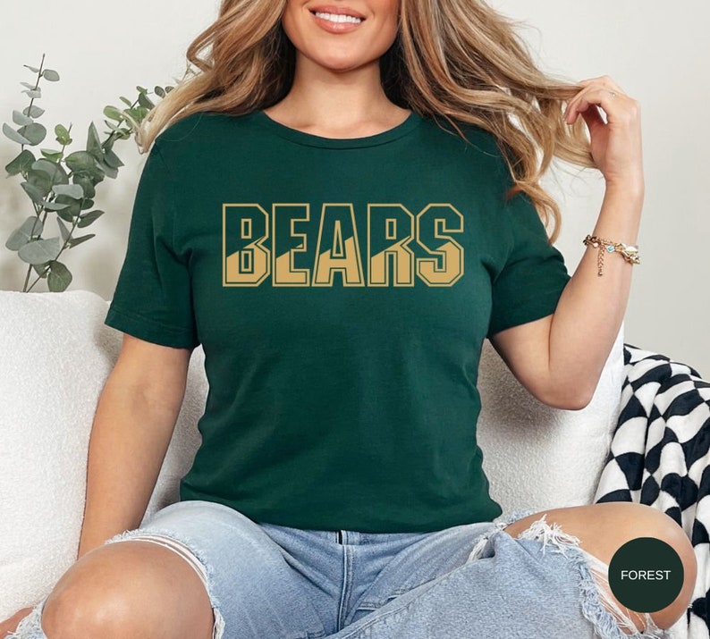 May include: A forest green t-shirt with the word "BEARS" printed in gold letters. The letters are outlined in black and have a mountain range design inside.