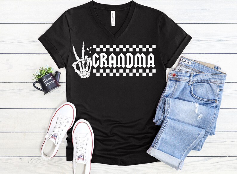 May include: Black v-neck t-shirt with a white graphic of a skeleton hand giving the peace sign and the word "Grandma" in a checkered pattern.