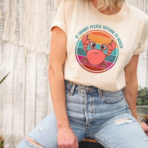 May include: A cream colored t-shirt with a retro-style graphic of a crab with the text "If Crabby Please Return to Beach".