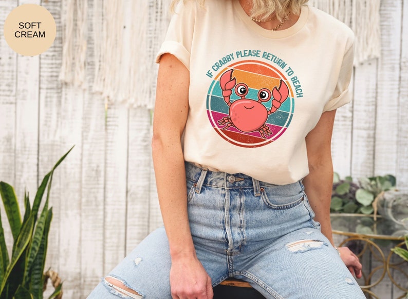 May include: A cream colored t-shirt with a retro-style graphic of a crab with the text "If Crabby Please Return to Beach".