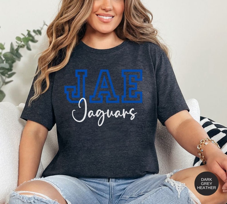 May include: A dark grey heather t-shirt with a blue outlined graphic of "JAE Jaguars" printed on the front.