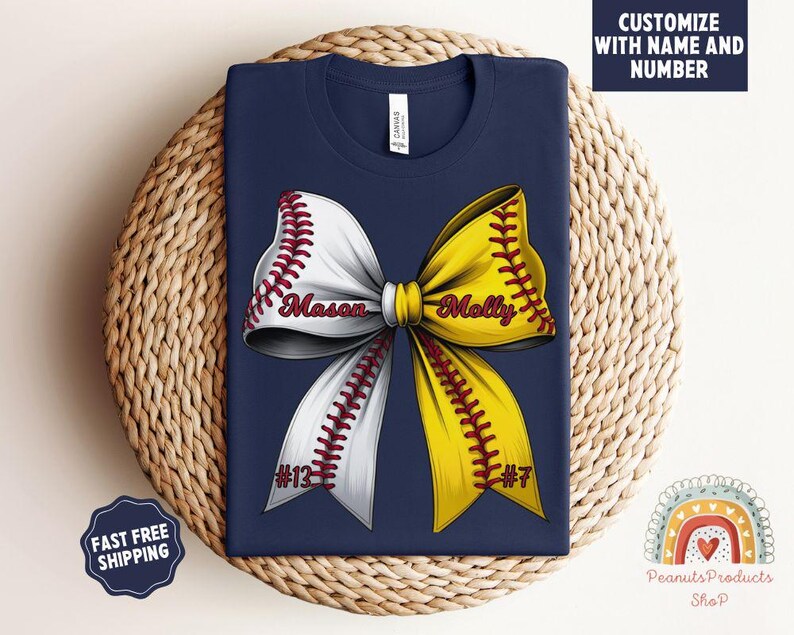 May include: Navy blue t-shirt with a white and yellow softball bow. The bow has red stitching and the names "Mason" and "Molly" with numbers "#13" and "#7" on each side.