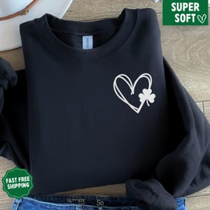 May include: Black sweatshirt featuring a white heart and shamrock design. The heart is drawn in a simple, hand-drawn style.
