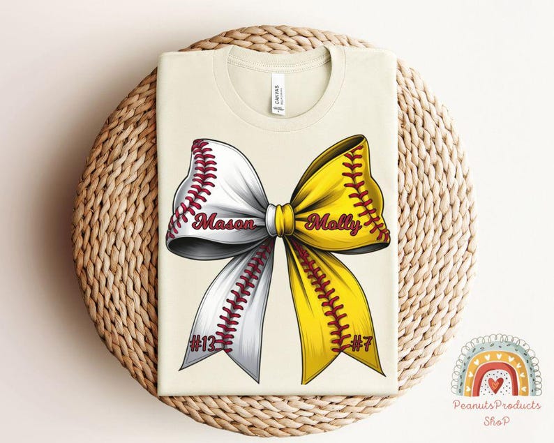 May include: A beige t-shirt with a softball bow design. The bow is white and yellow with red stitching. The words "Mason #12" and "Molly #7" are written on the bow.
