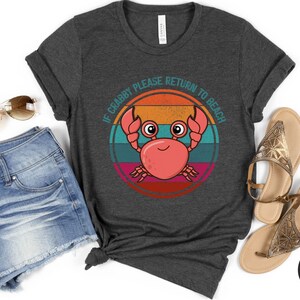 May include: Dark grey heather t-shirt with a retro-style graphic of a crab with the text "If Crabby Please Return to Beach".