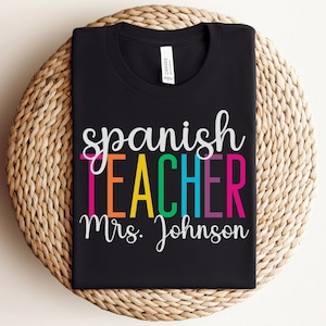 K&ouml;nnte beinhalten: Schwarzes T-Shirt mit dem Text "spanish teacher mrs. Johnson" in Regenbogenfarben.