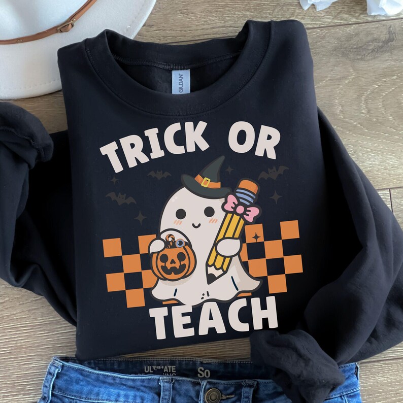 May include: Black sweatshirt with a white graphic of a ghost holding a pencil and a pumpkin. The text "Trick or Teach" is printed on the sweatshirt.