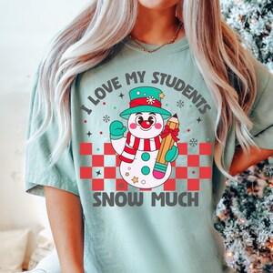 May include: A teal blue t-shirt with a snowman holding a pencil and the text "I love my students snow much".