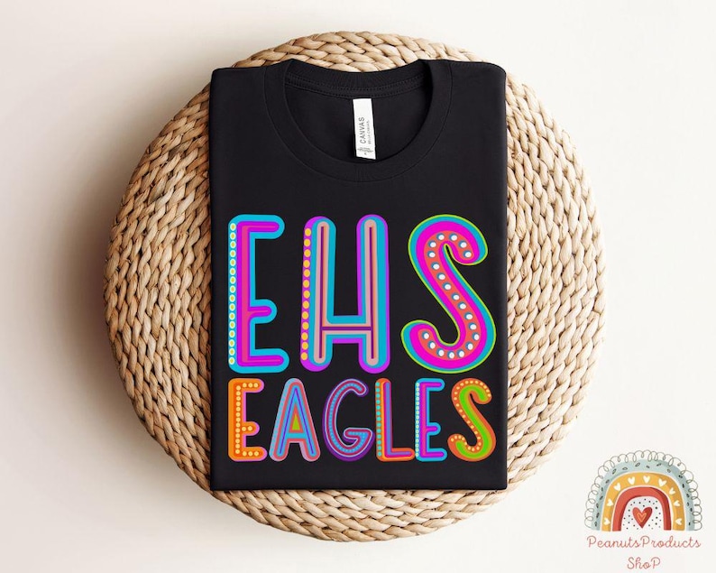 Puede incluir: Camiseta negra con el texto "EHS Eagles" en letras de colores y contorneadas. Las letras est&aacute;n decoradas con peque&ntilde;os puntos de colores.