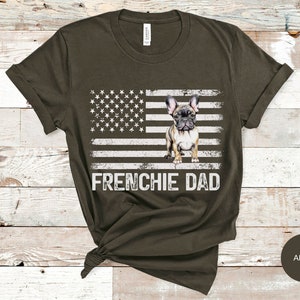 May include: A dark green t-shirt with a white American flag and a French bulldog standing in front of it. The text "FRENCHIE DAD" is printed below the flag.