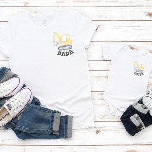 Peut inclure: T-shirts blancs et un body pour b&eacute;b&eacute; avec un dessin de pelle m&eacute;canique jaune et les mots "DADA" et "SISTER". Les chemises sont associ&eacute;es &agrave; des jeans bleus et des baskets blanches avec des d&eacute;tails rouges.