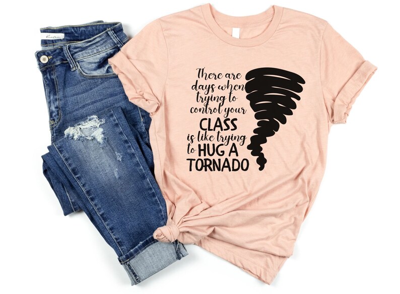 May include: A peach-colored t-shirt with black text that reads "There are days when trying to control your CLASS is like trying to HUG A TORNADO". A black tornado graphic is on the right side of the shirt.