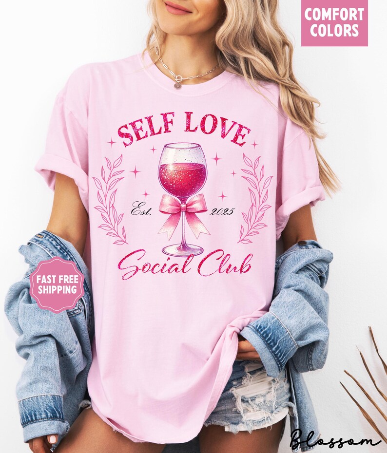 May include: Pink t-shirt with the text "Self Love Social Club" and a glass of wine with a pink bow. The text "Est. 2023" is below the wine glass.